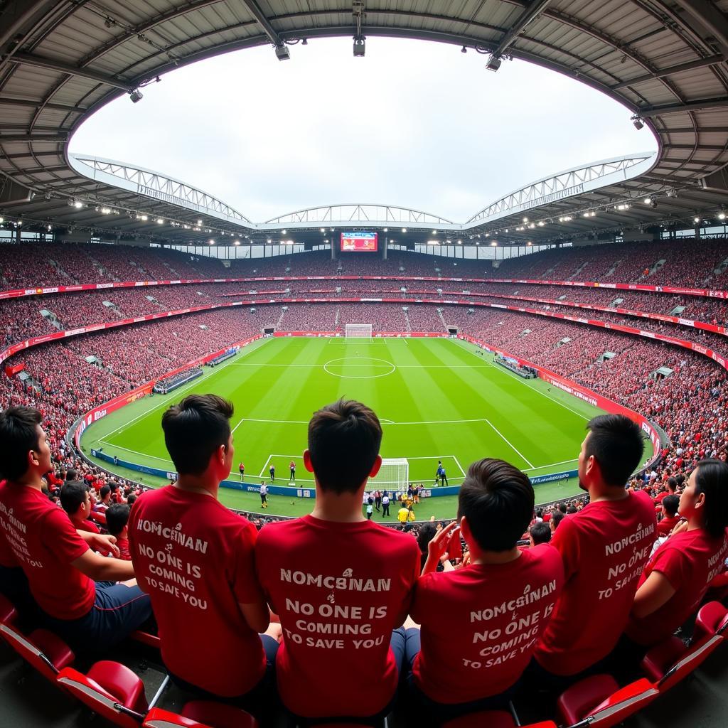 Wide shot of the stadium crowd with many fans wearing "No One Is Coming To Save You" shirts, creating a sea of support for "Đội Bóng Đá."